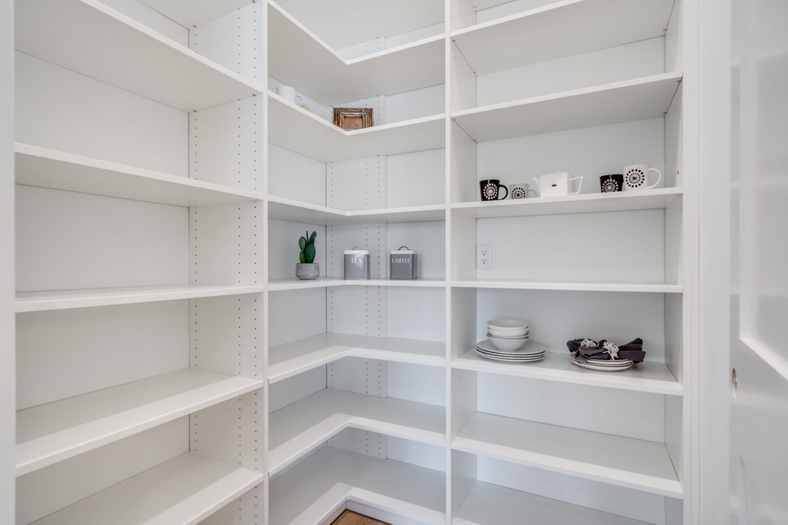 A white pantry with many shelves and dishes.